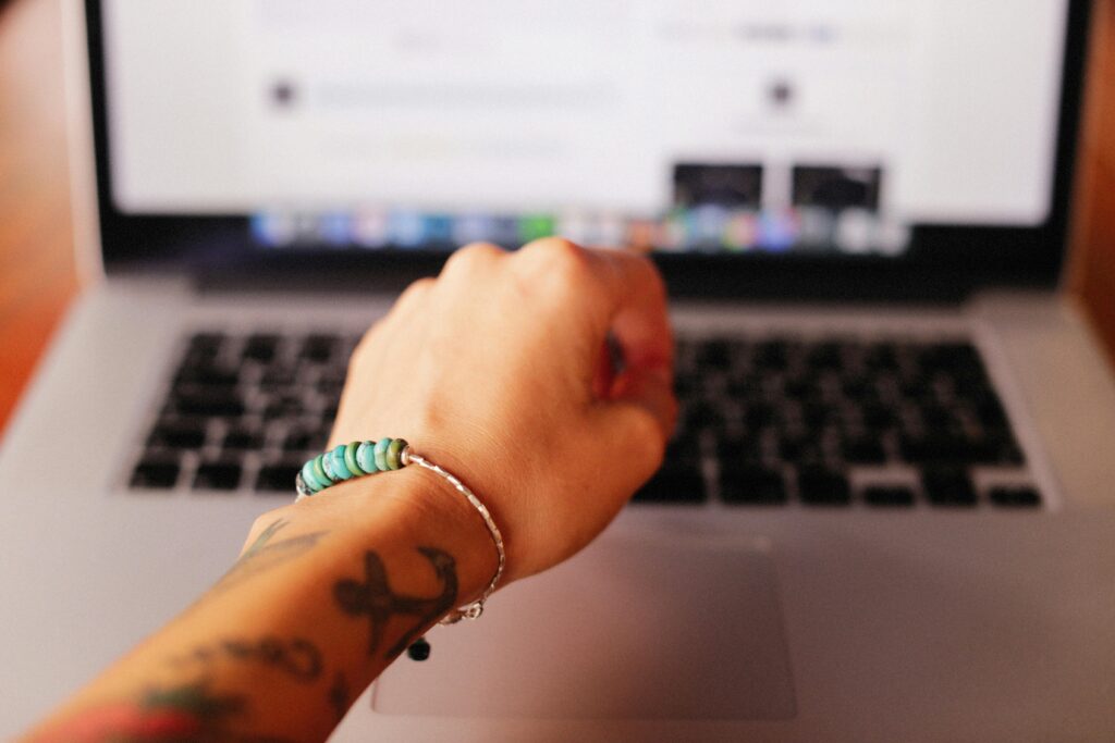 Close-up of a tattooed hand wearing a bracelet typing on a laptop.
